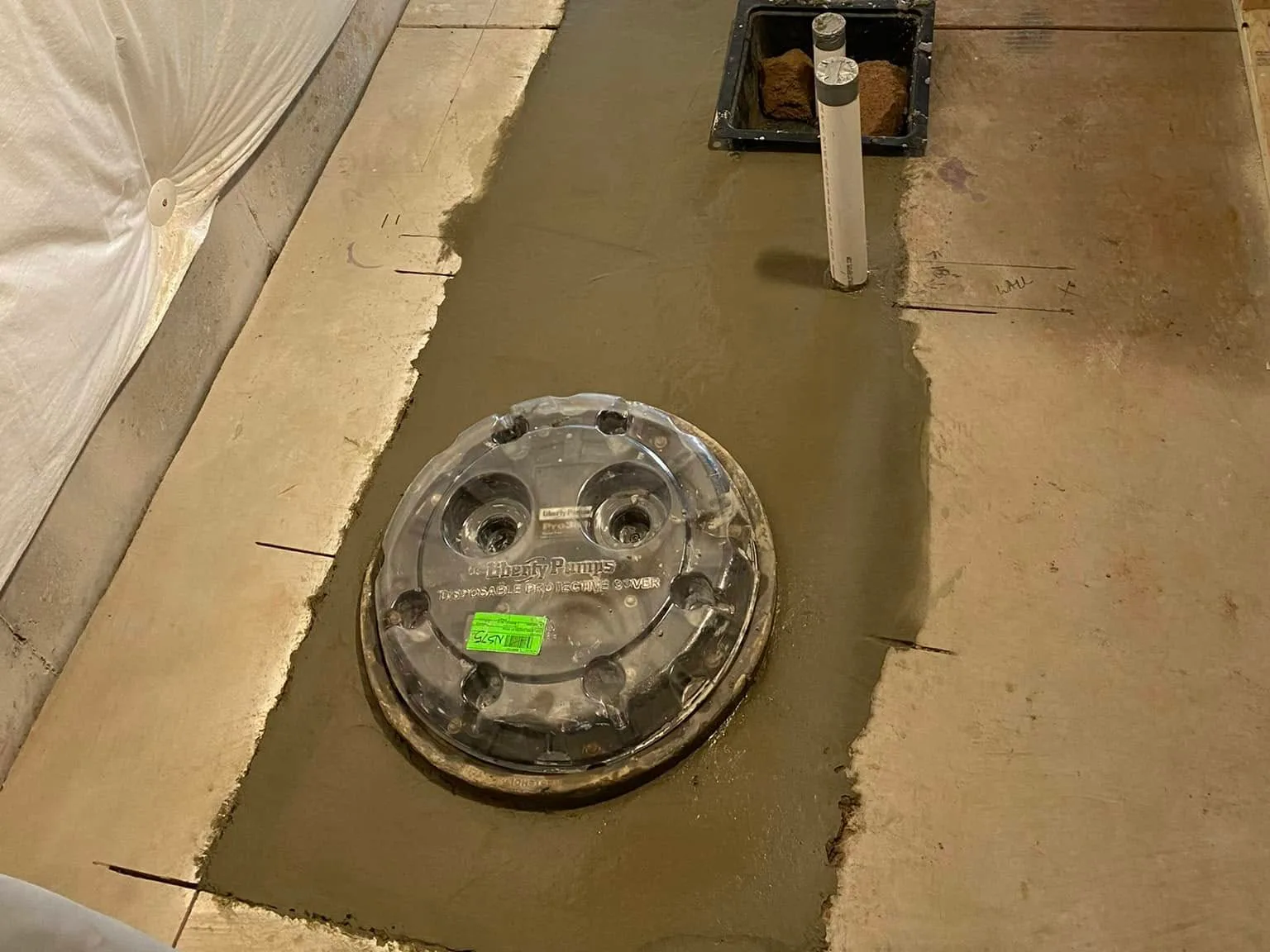 The same floor patched with concrete, with the drain stubs, the shower drain box and the ejector basin cover in place