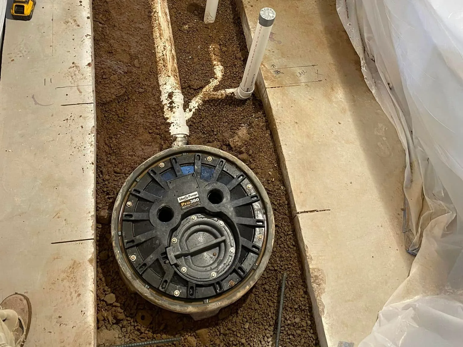A basement floor cut open for a new bathroom: new drain lines and a sewage ejector basin set in the trench