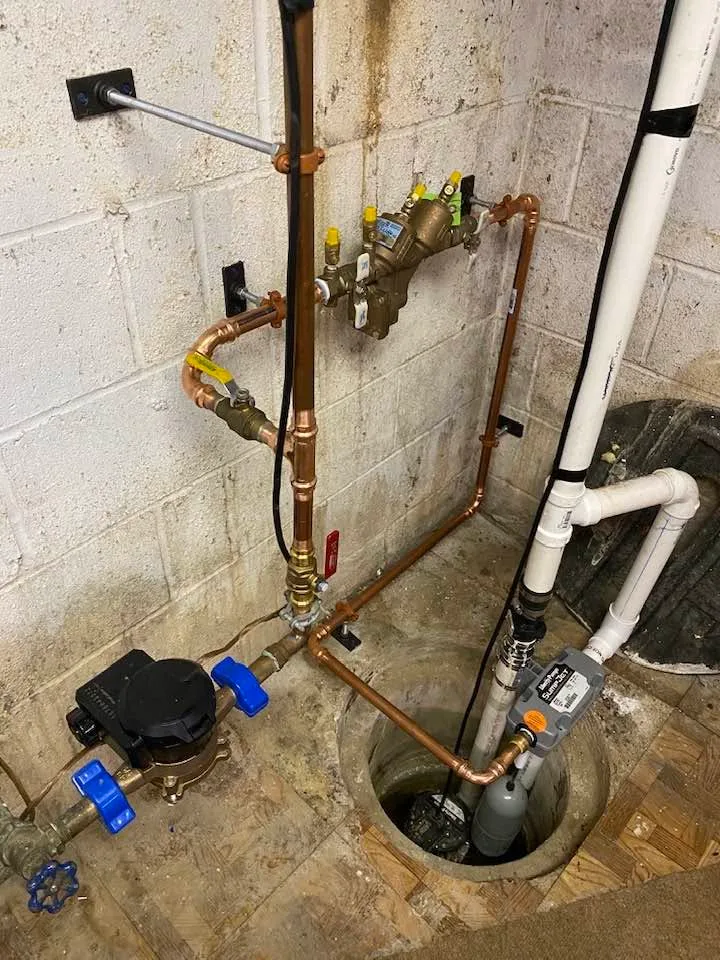 A new copper water service in a basement, with a backflow preventer, a water meter and a sump pump